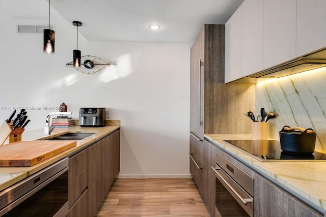 kitchen with decorative light fixtures, white cabinetry, backsplash, stainless steel oven, and light hardwood / wood-style floors