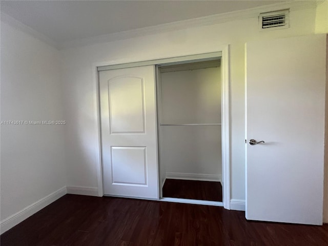 unfurnished bedroom featuring crown molding, dark hardwood / wood-style flooring, and a closet