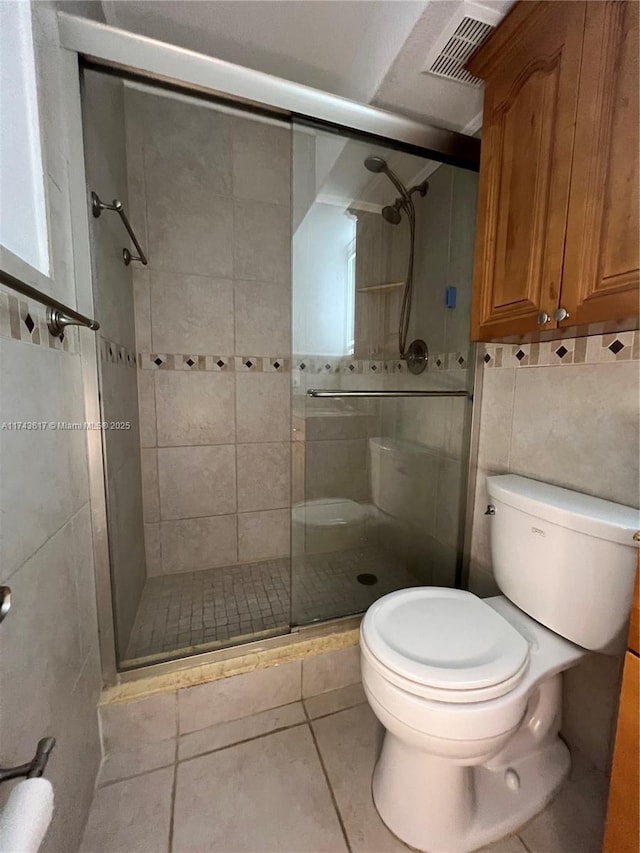 bathroom featuring toilet, a shower with shower door, tile patterned flooring, and tile walls