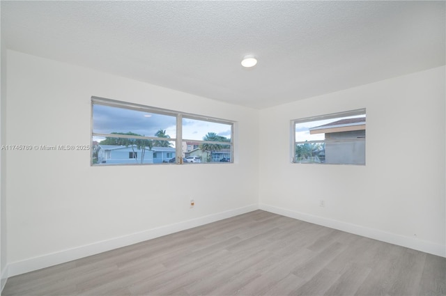 unfurnished room with plenty of natural light, baseboards, light wood-style flooring, and a textured ceiling