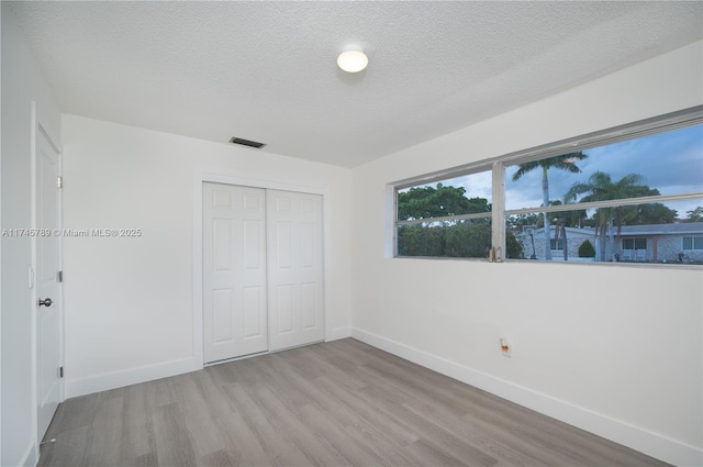 unfurnished bedroom featuring light wood-style flooring, a closet, visible vents, and baseboards