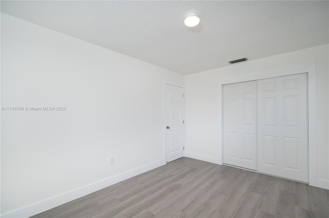 unfurnished bedroom featuring a closet, visible vents, light wood-style flooring, and baseboards