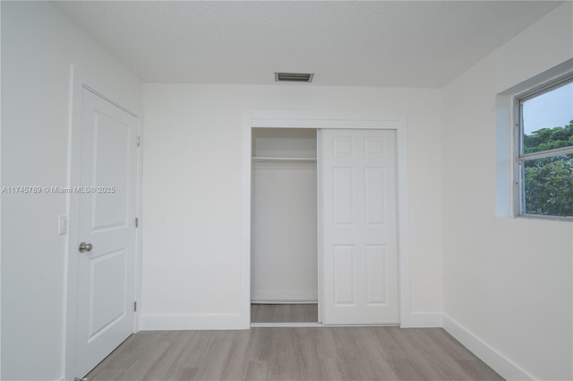 unfurnished bedroom featuring a closet, visible vents, a textured ceiling, light wood-type flooring, and baseboards