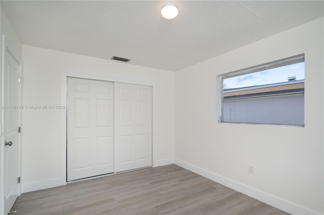 unfurnished bedroom with a textured ceiling, light wood-style flooring, visible vents, and baseboards