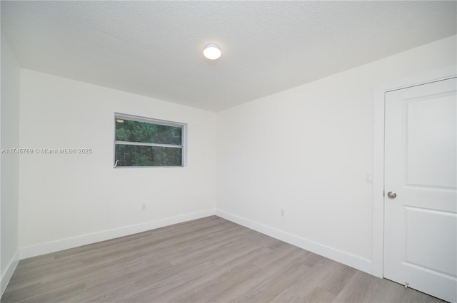 empty room with a textured ceiling, light wood-style flooring, and baseboards