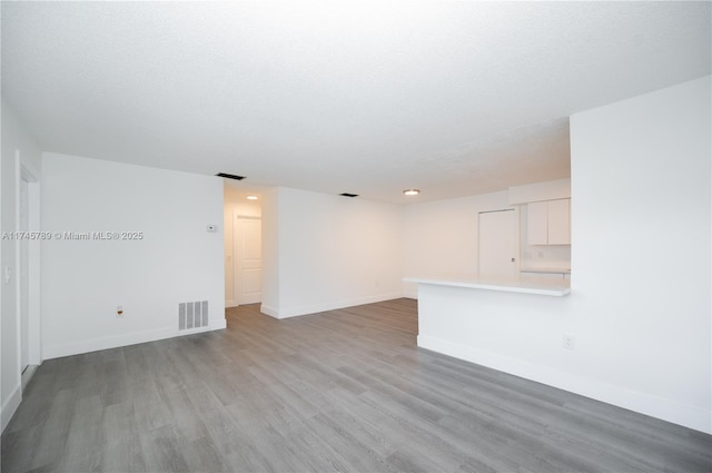 empty room featuring visible vents, light wood-style flooring, baseboards, and a textured ceiling