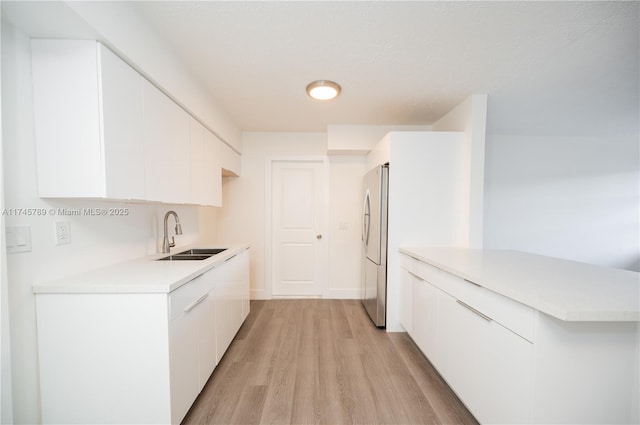 kitchen with light countertops, freestanding refrigerator, a sink, and white cabinetry