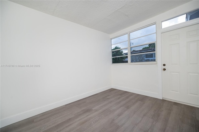 unfurnished room featuring a textured ceiling, baseboards, and wood finished floors