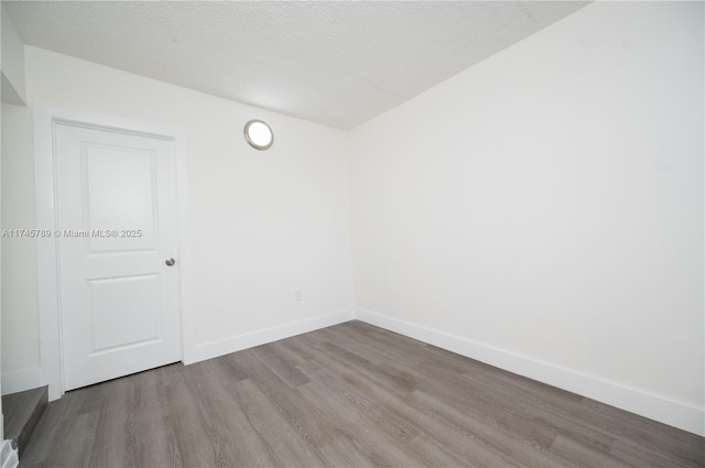 unfurnished room with a textured ceiling, baseboards, and wood finished floors