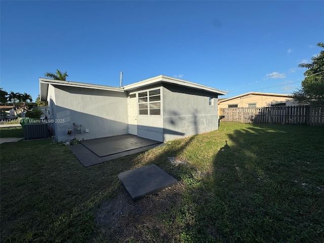 rear view of property with a lawn, fence, central air condition unit, a patio area, and stucco siding