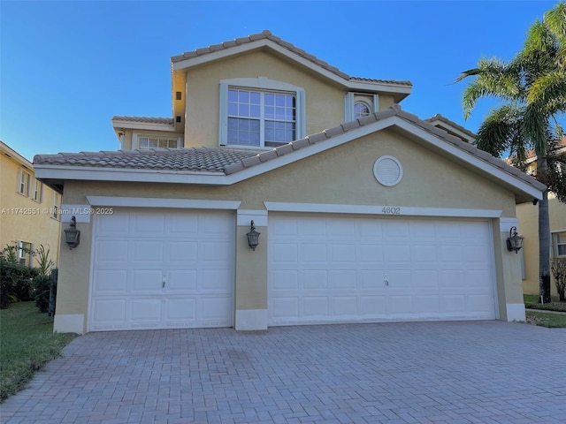 traditional-style home with a garage, decorative driveway, stucco siding, and a tiled roof