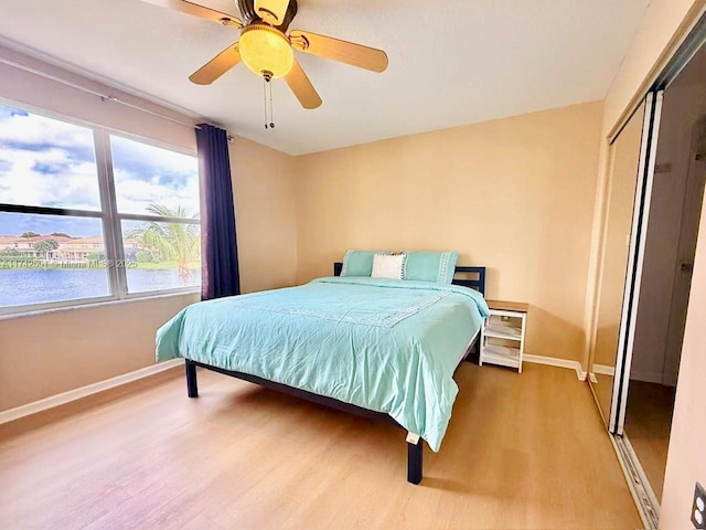bedroom with ceiling fan, baseboards, wood finished floors, a water view, and a closet