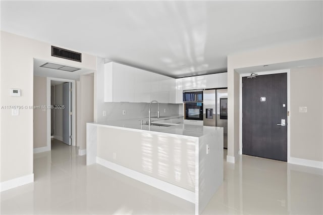 kitchen featuring sink, stainless steel fridge with ice dispenser, light tile patterned floors, white cabinets, and backsplash