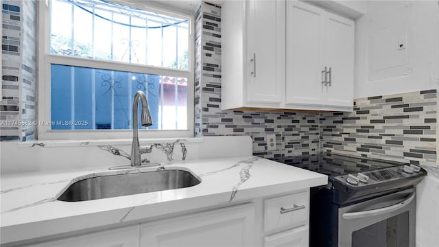 kitchen with sink, white cabinetry, light stone countertops, decorative backsplash, and stainless steel range with electric cooktop