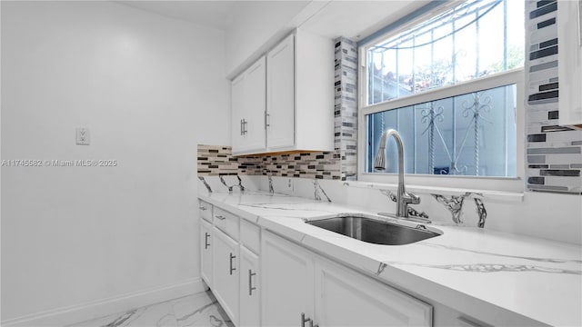 kitchen featuring white cabinetry, sink, light stone counters, and decorative backsplash