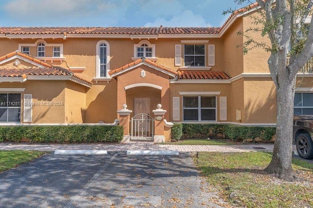 view of front of home featuring uncovered parking, a gate, a tile roof, and stucco siding