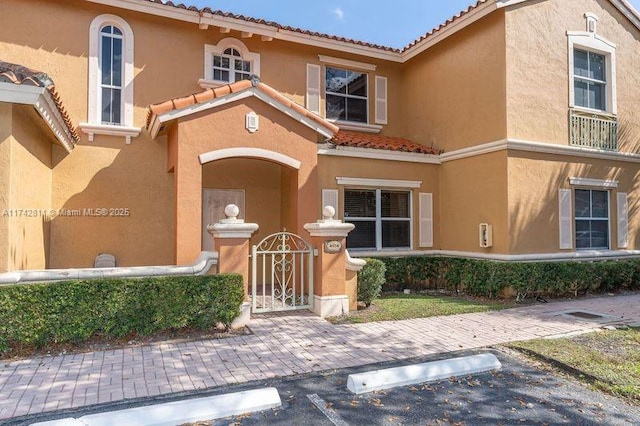 view of front of home featuring uncovered parking, a gate, a tiled roof, and stucco siding