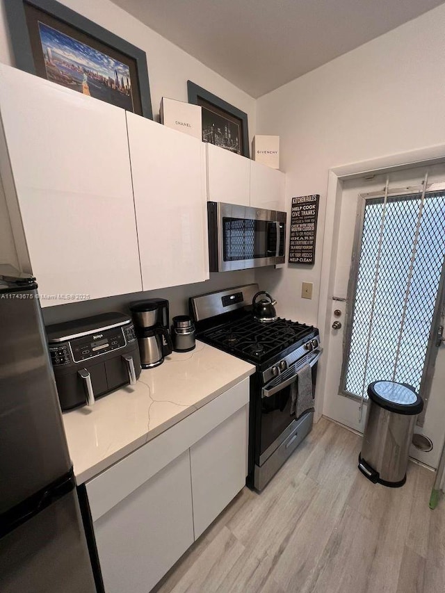 kitchen with white cabinetry, stainless steel appliances, light stone countertops, and light hardwood / wood-style floors