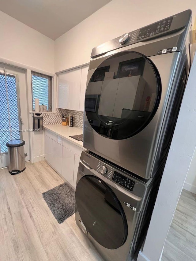 laundry area featuring cabinets, stacked washer / dryer, and light hardwood / wood-style floors