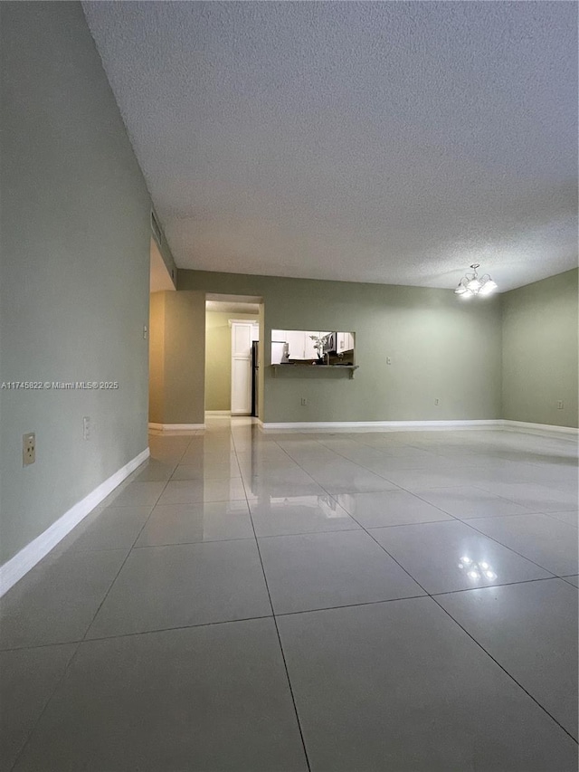 tiled empty room with a chandelier and a textured ceiling