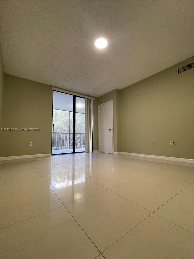 spare room featuring tile patterned flooring, a textured ceiling, and a wall of windows