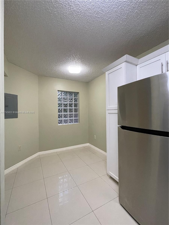 interior space featuring stainless steel refrigerator, light tile patterned floors, a textured ceiling, and white cabinets