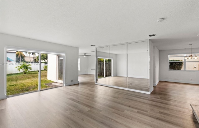 unfurnished bedroom with an inviting chandelier, hardwood / wood-style floors, a textured ceiling, and access to exterior