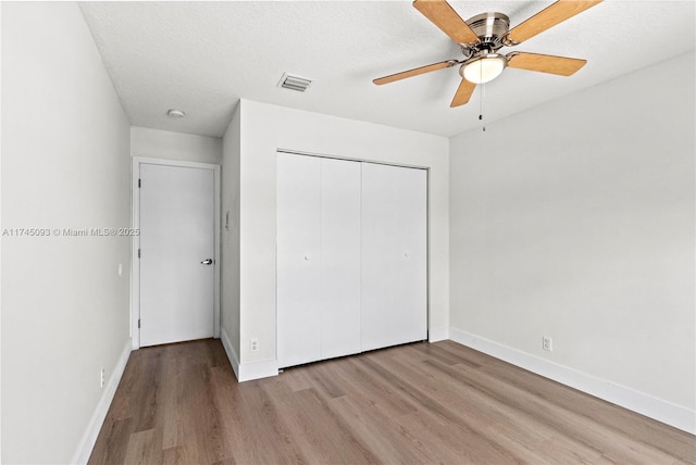 unfurnished bedroom with ceiling fan, a closet, light hardwood / wood-style flooring, and a textured ceiling