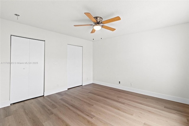 unfurnished bedroom with ceiling fan, light hardwood / wood-style floors, and multiple closets