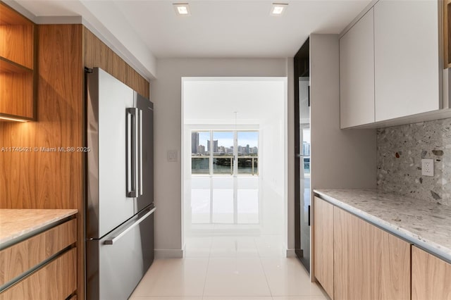 kitchen featuring high quality fridge, tasteful backsplash, white cabinetry, light tile patterned floors, and light stone counters