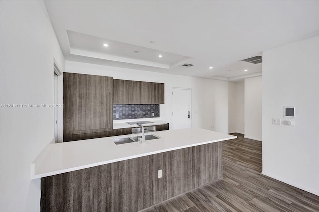 kitchen featuring sink, a tray ceiling, dark hardwood / wood-style floors, kitchen peninsula, and decorative backsplash