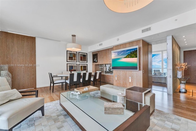 living room with light wood-style floors, recessed lighting, visible vents, and wooden walls