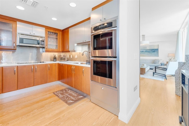 kitchen featuring a sink, visible vents, light countertops, appliances with stainless steel finishes, and glass insert cabinets