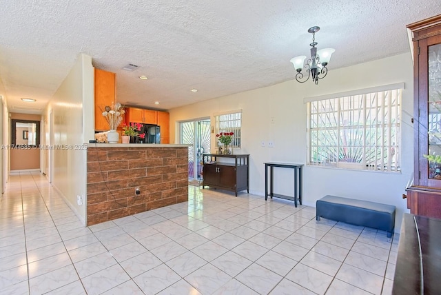 kitchen with visible vents, a textured ceiling, freestanding refrigerator, light tile patterned flooring, and a chandelier