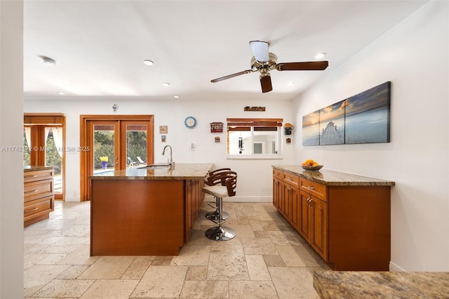 kitchen with sink, a breakfast bar area, dark stone counters, a center island with sink, and french doors