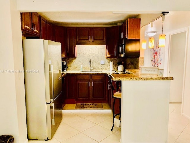 kitchen with a kitchen bar, sink, light stone counters, hanging light fixtures, and white refrigerator