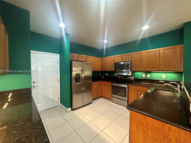 kitchen featuring appliances with stainless steel finishes, sink, dark stone countertops, and light tile patterned floors