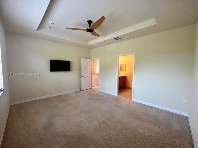 unfurnished bedroom with ceiling fan, light colored carpet, connected bathroom, and a tray ceiling