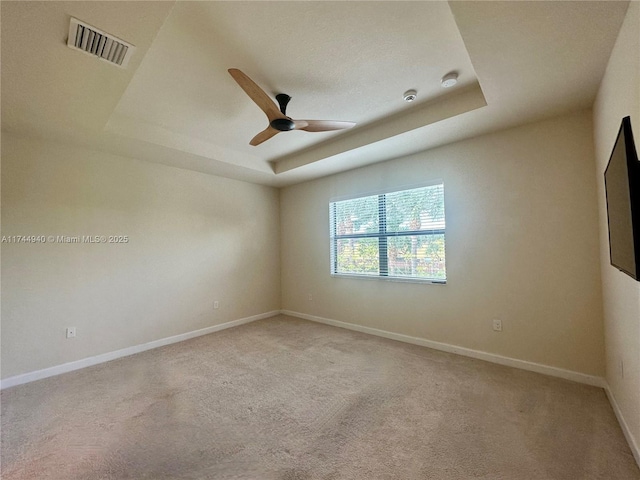 carpeted empty room with a raised ceiling and ceiling fan