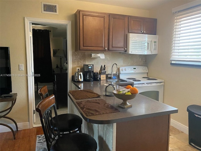 kitchen with a sink, white appliances, backsplash, baseboards, and visible vents