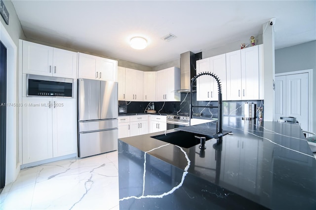 kitchen featuring white cabinets, backsplash, stainless steel counters, stainless steel appliances, and wall chimney exhaust hood