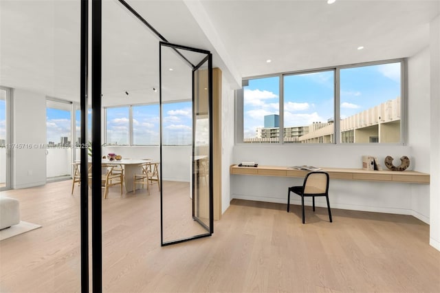 home office with a wealth of natural light, built in desk, and light hardwood / wood-style floors