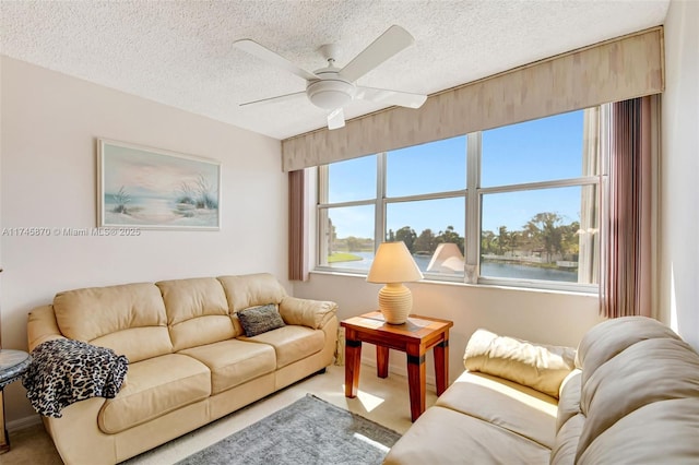 carpeted living room with ceiling fan, a water view, and a textured ceiling