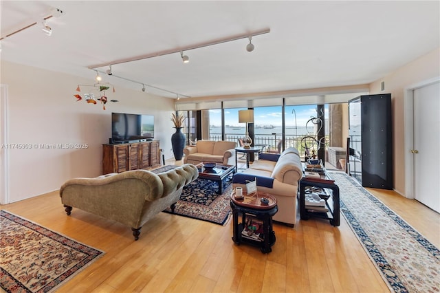 living room with a wall of windows, track lighting, and light wood-type flooring