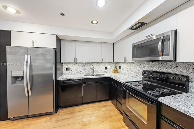 kitchen with sink, white cabinetry, light hardwood / wood-style flooring, decorative backsplash, and black appliances