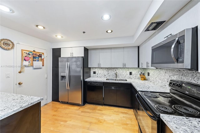 kitchen with sink, decorative backsplash, black appliances, light stone countertops, and light hardwood / wood-style flooring