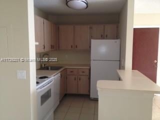 kitchen featuring white appliances, kitchen peninsula, sink, and light tile patterned floors