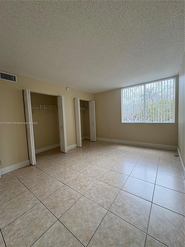 10717 Cleary Blvd Unit 203, Plantation, FL 33324 - unfurnished bedroom featuring a textured ceiling, light tile patterned floors, visible vents, baseboards, and two closets