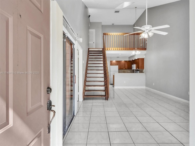 tiled entryway with ceiling fan and a towering ceiling