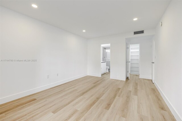 unfurnished bedroom featuring a walk in closet, baseboards, and light wood-type flooring